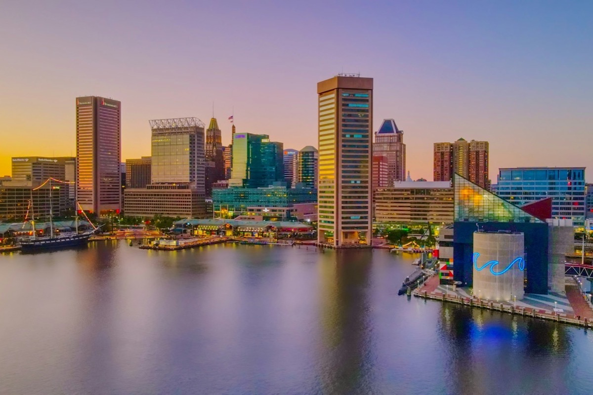 The Baltimore Inner Harbor skyline at sunset, with the World Trade Center tower, the USS Constellation, and the National Aquarium reflected in the water