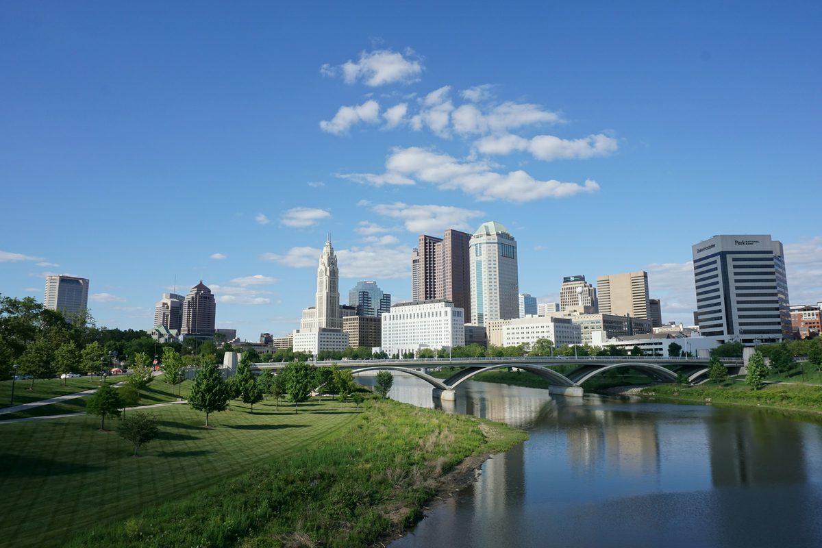 The downtown Columbus, Ohio skyline on a clear day, with LeVeque Tower rising above the Scioto River and a bridge along the Scioto Mile
