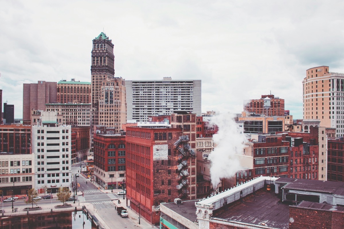 An elevated view of downtown Detroit, with the green copper crown of Book Tower rising above red brick buildings and a plume of rooftop steam