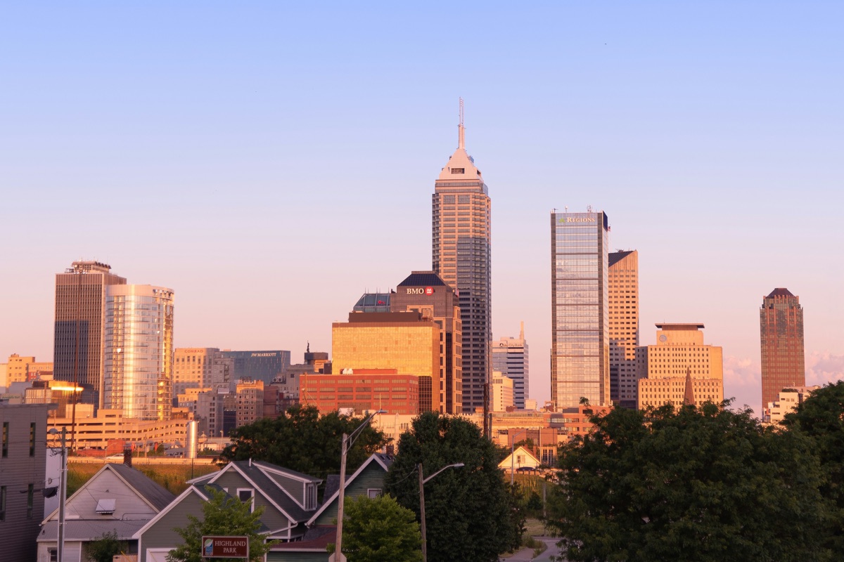 The downtown Indianapolis skyline at golden hour, with Salesforce Tower rising above the other high-rises and rooftops and trees in the foreground