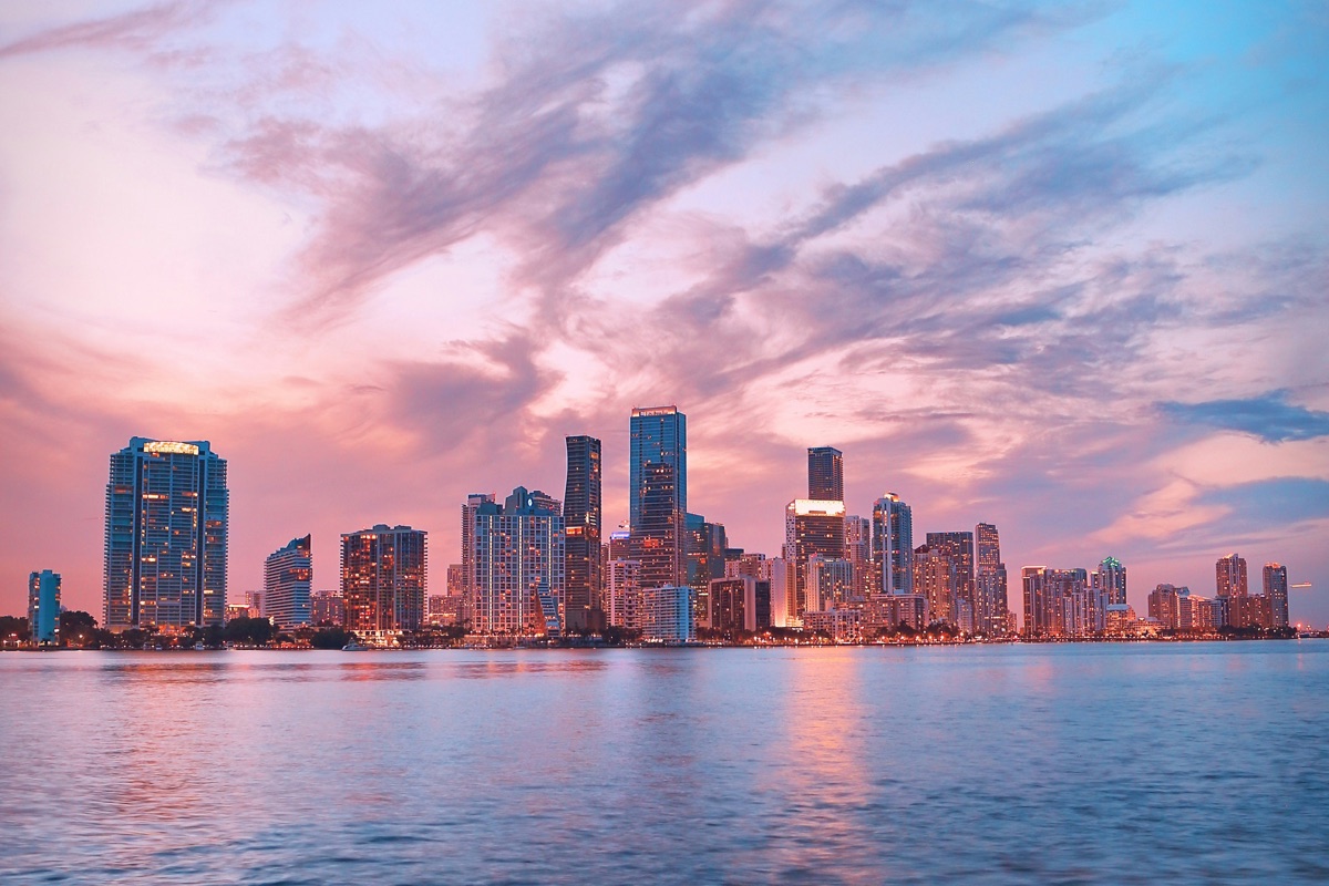 Miami skyline at sunset across Biscayne Bay, with downtown and Brickell towers reflecting in the water
