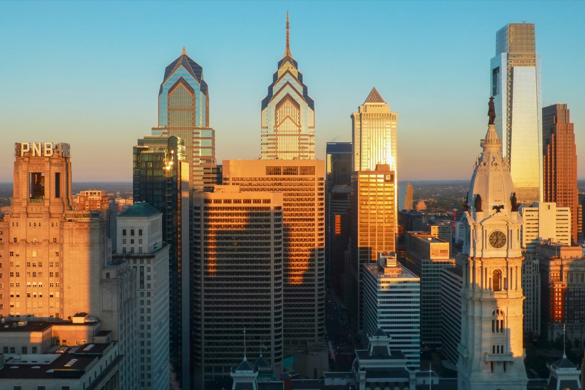 Center City Philadelphia at golden hour, with the clock tower and William Penn statue of City Hall in front of Liberty Place and the Comcast Center