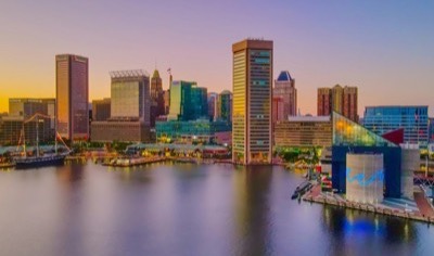 The Baltimore Inner Harbor skyline at sunset, with the World Trade Center tower, the USS Constellation, and the National Aquarium reflected in the water