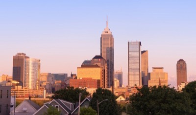 The downtown Indianapolis skyline at golden hour, with Salesforce Tower rising above the other high-rises and rooftops and trees in the foreground