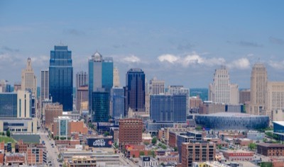 The downtown Kansas City, Missouri skyline on a clear day, with blue glass towers rising above red brick buildings and the round T-Mobile Center arena on the right